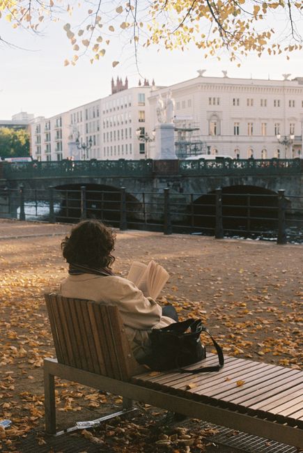 Woman reading on a bench by a canal in an autumn cityscape.