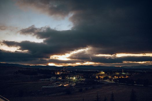 A dramatic evening sky with clouds and distant town lights create a serene landscape.