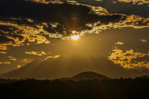 Free Golden sunset casting dramatic shadows over mountain peaks with stunning cloud formations. Stock Photo