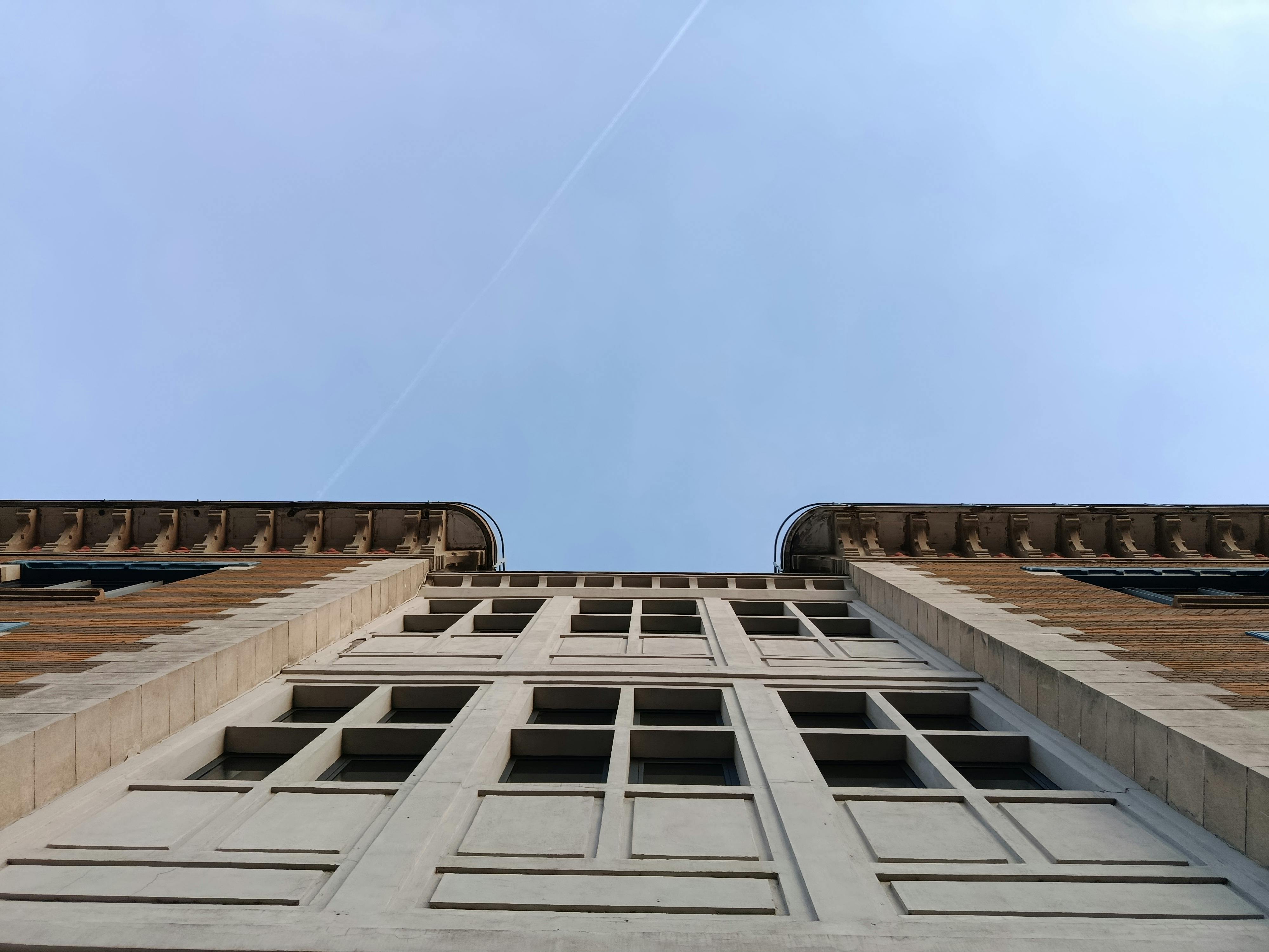 Gratis Suggestiva vista dal basso di un grattacielo con architettura simmetrica sullo sfondo di un cielo azzurro e terso. Foto a disposizione