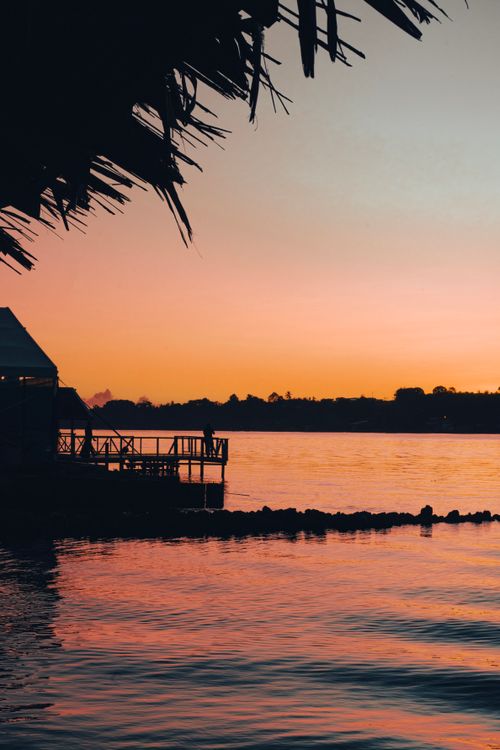Free A picturesque lakeside view at sunset featuring silhouetted structures and vibrant colors. Stock Photo