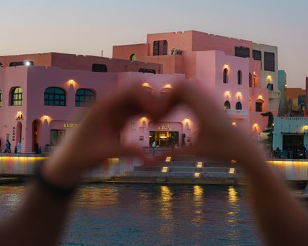 Colorful buildings reflecting traditional Qatari architecture with a heart gesture in the foreground.