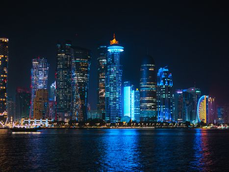 Dramatic nighttime view of Doha skyline with illuminated modern skyscrapers reflecting on the water.