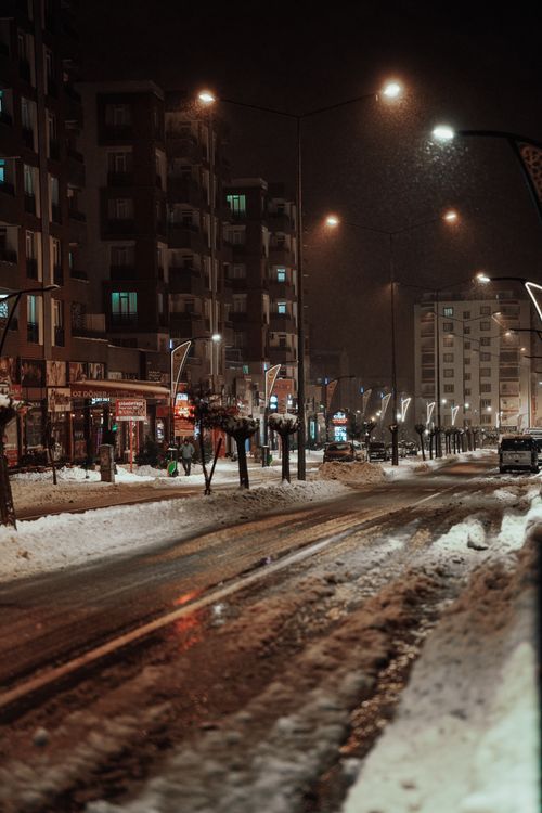 Free Snow-covered urban street at night, illuminated by glowing streetlights. Stock Photo