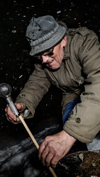 A senior man wearing a coat and hat works diligently outdoors in a snowy winter night.