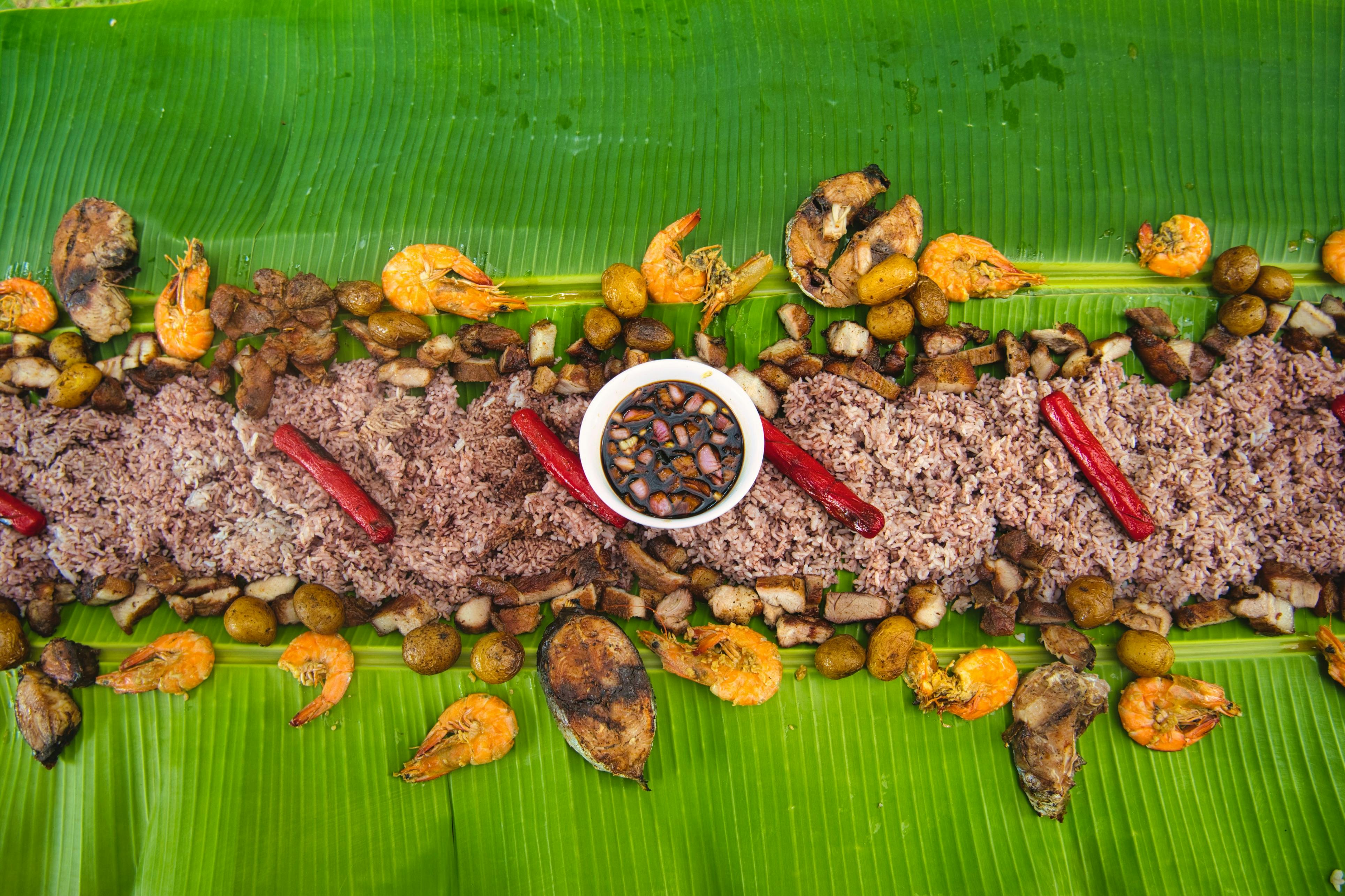 Vibrant Filipino boodle fight spread with rice, shrimp, and vegetables on banana leaves.