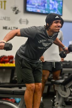A young man exercising with dumbbells at an indoor gym, focused on fitness and strength training.