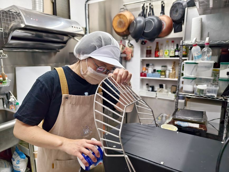 キッチンエプロンとキャップを着けたシェフが、プロのキッチン環境で器具を準備します。