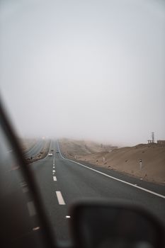 Moody image of a fog-covered desert highway, viewed from a car window, suggesting adventure and solitude.