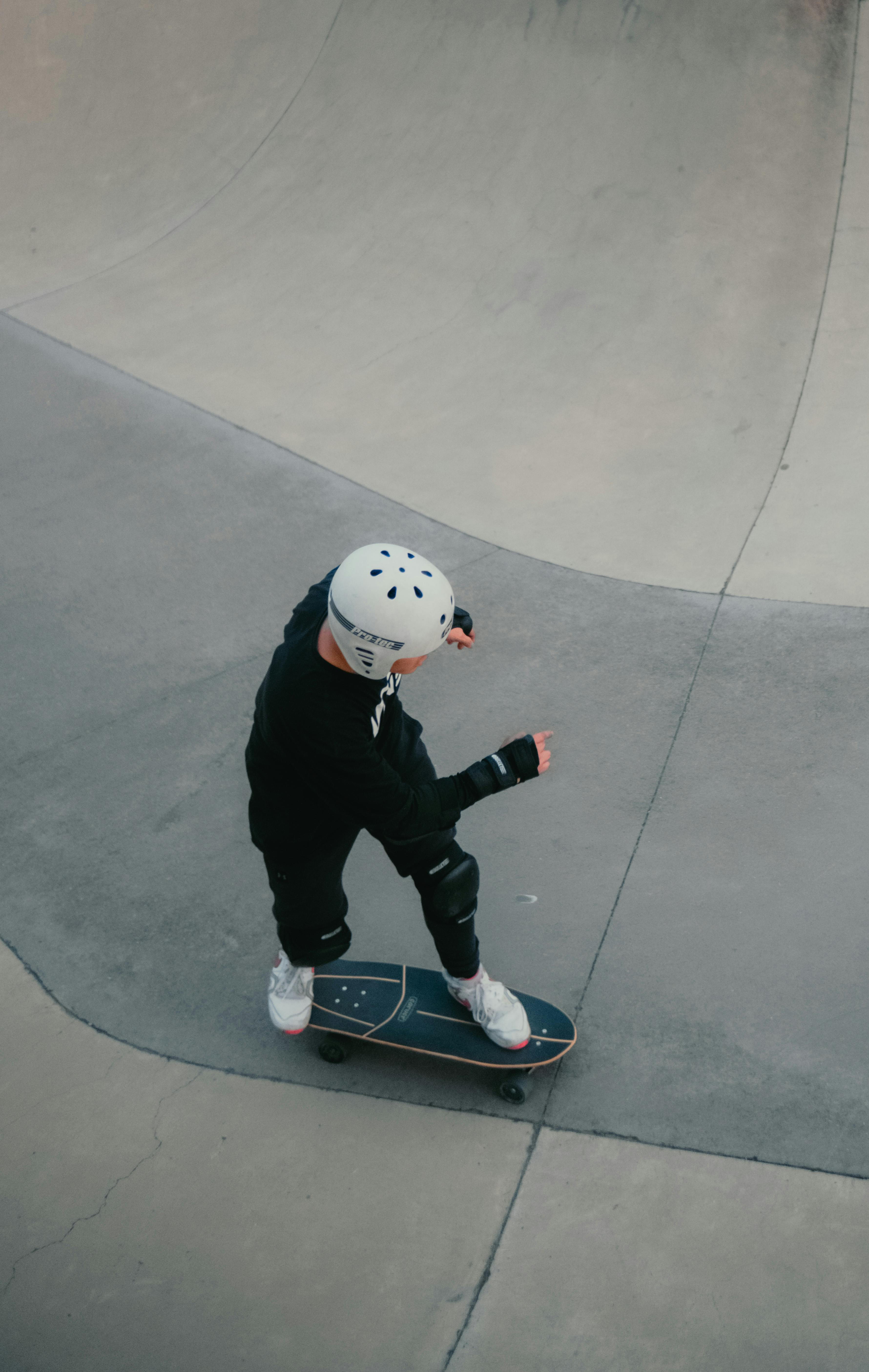 Gratuit Un jeune skateur réalise des figures dans un skatepark en béton, portant un équipement de protection. Photos