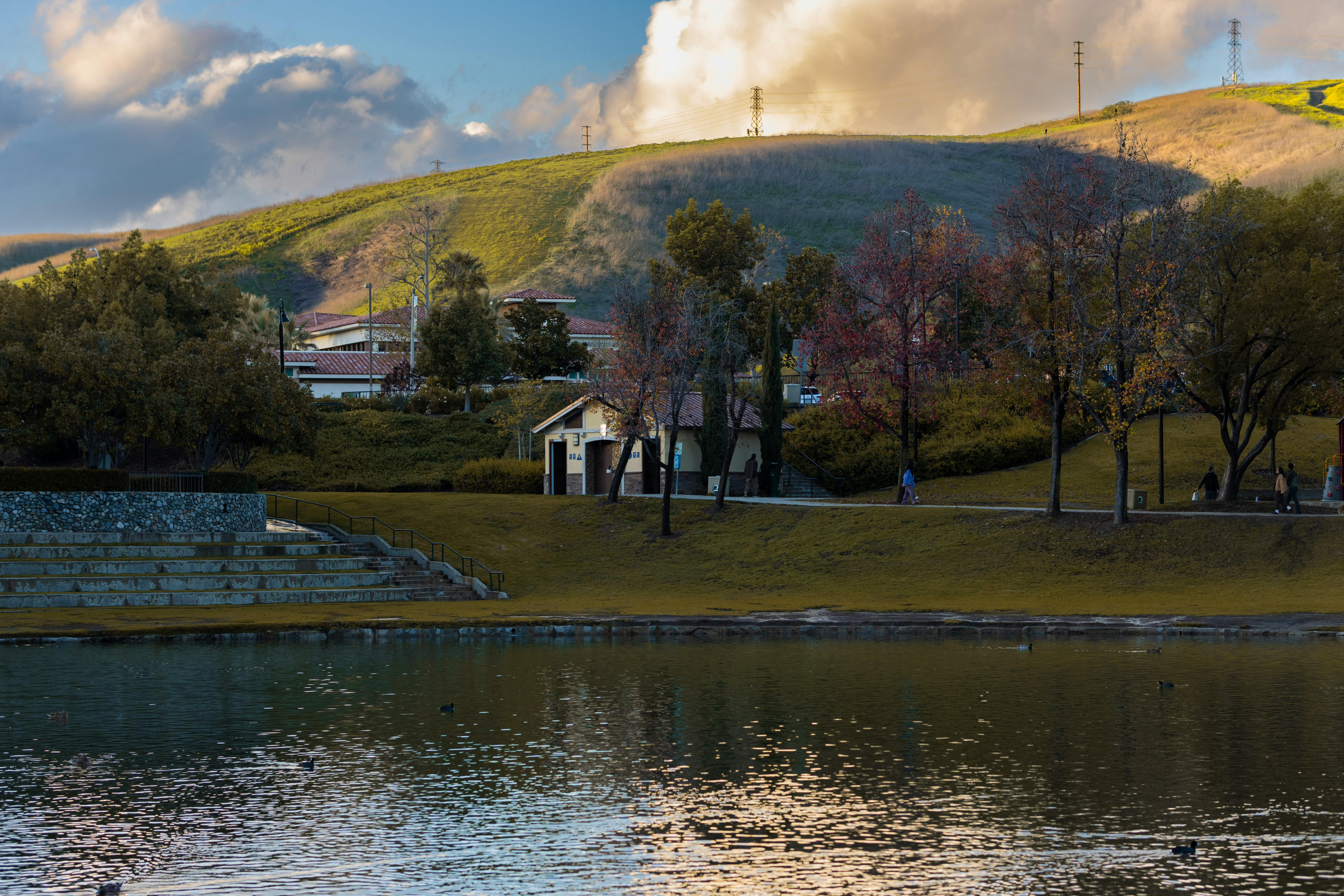 Beautiful park with tranquil lake, trees, and hills under a cloudy sky in the afternoon.
