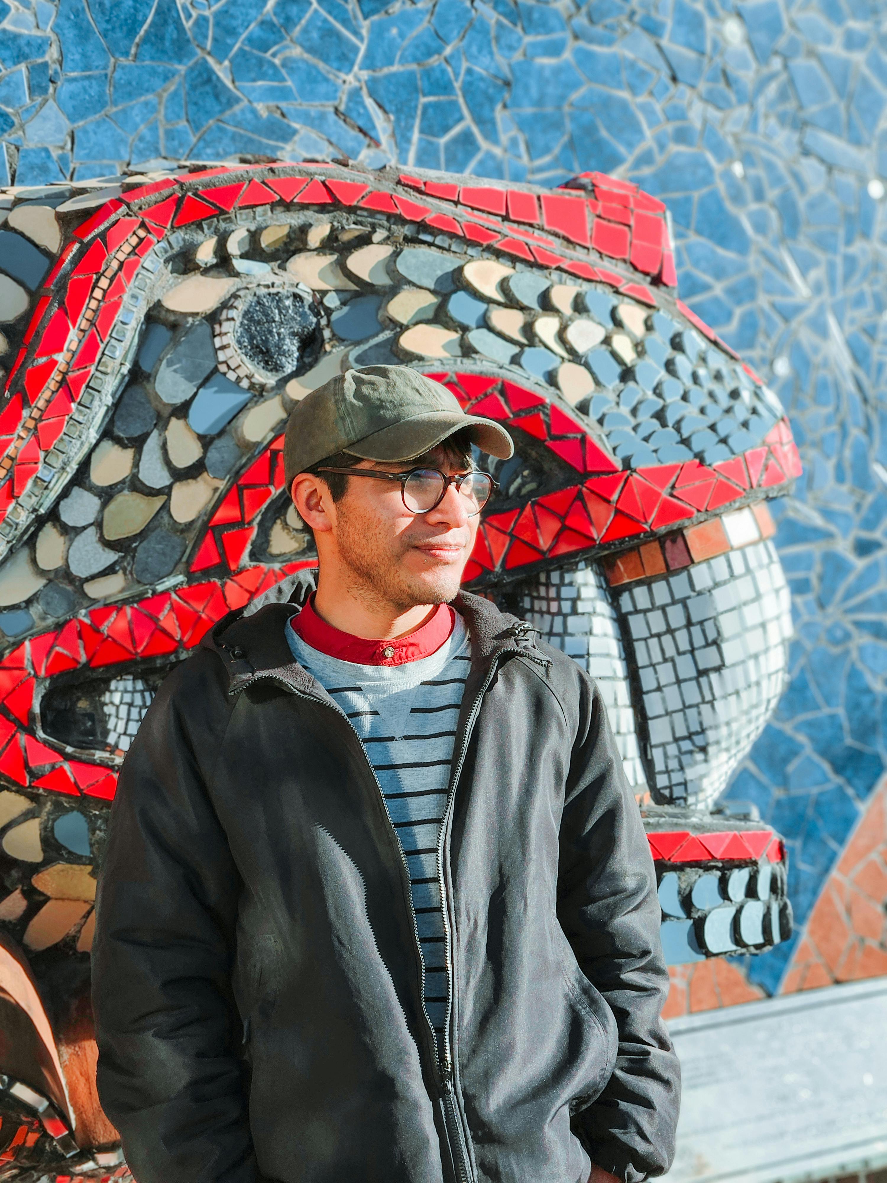 De franc Un jove està somrient contra una paret de mosaic intricat i colorit en un dia assolellat. Foto d'estoc