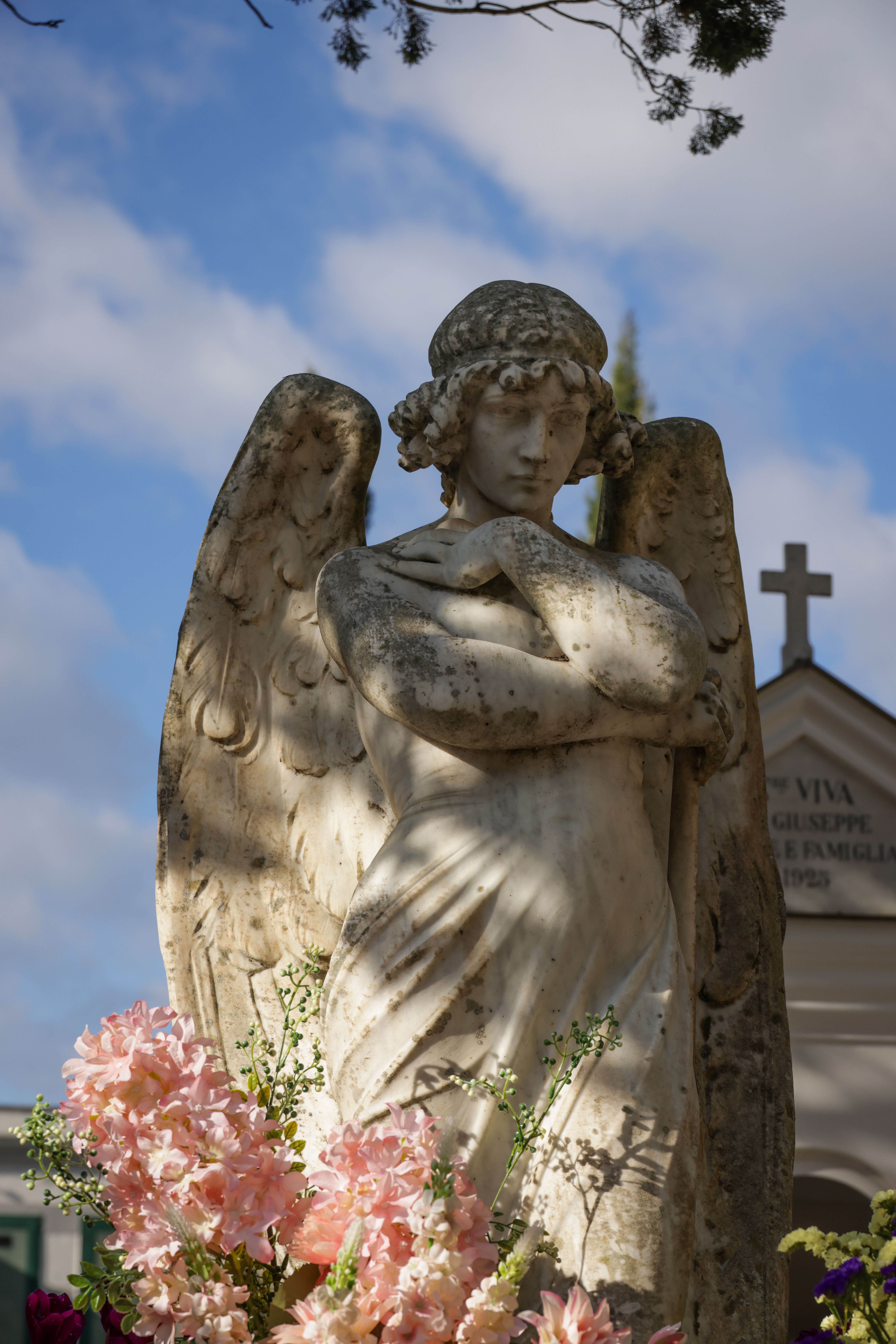 A tranquil angel statue surrounded by flowers in a sunlit cemetery, embodying peace and remembrance.