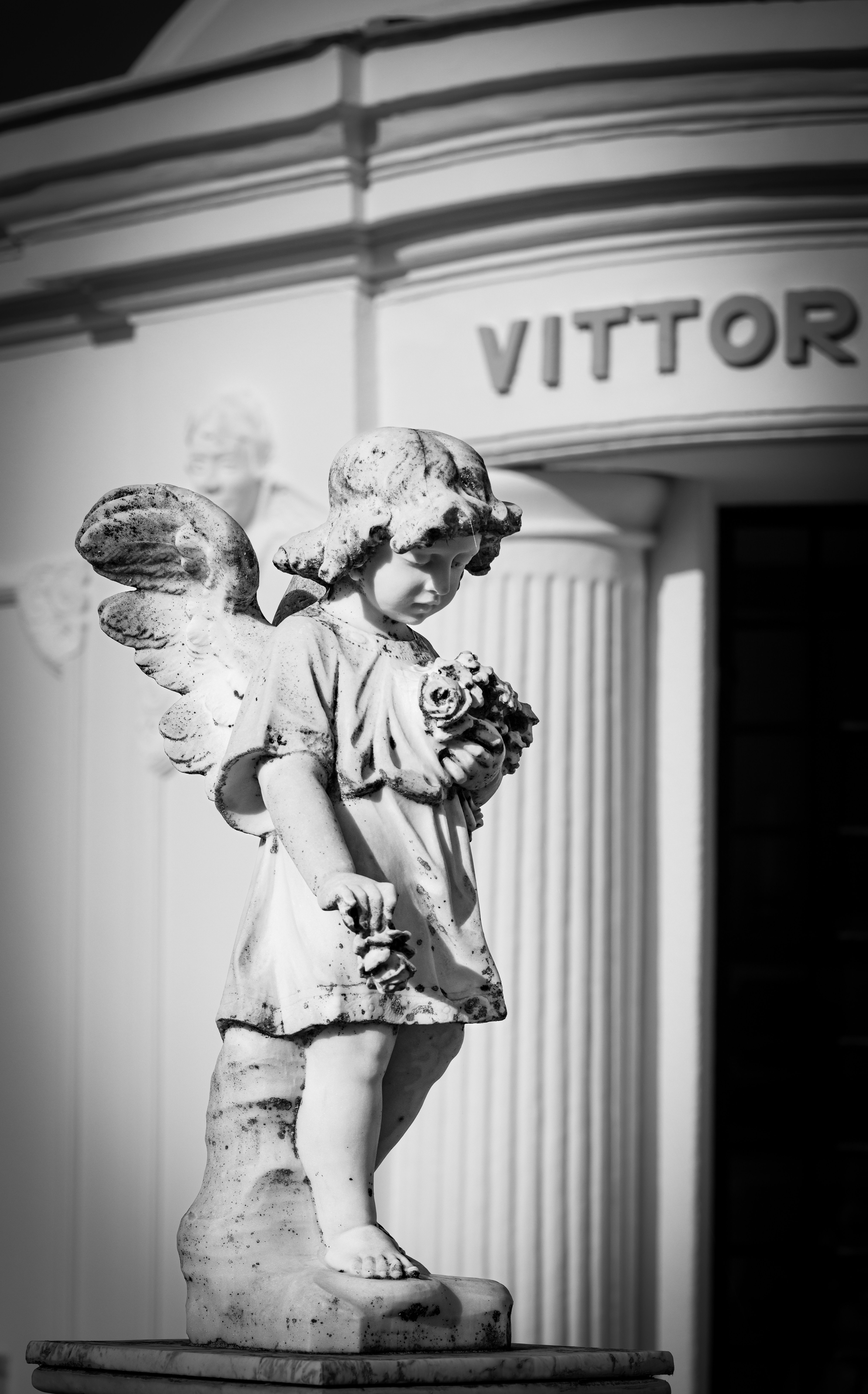 A black and white photo of an angel statue at a cemetery entrance, conveying peace and spirituality.