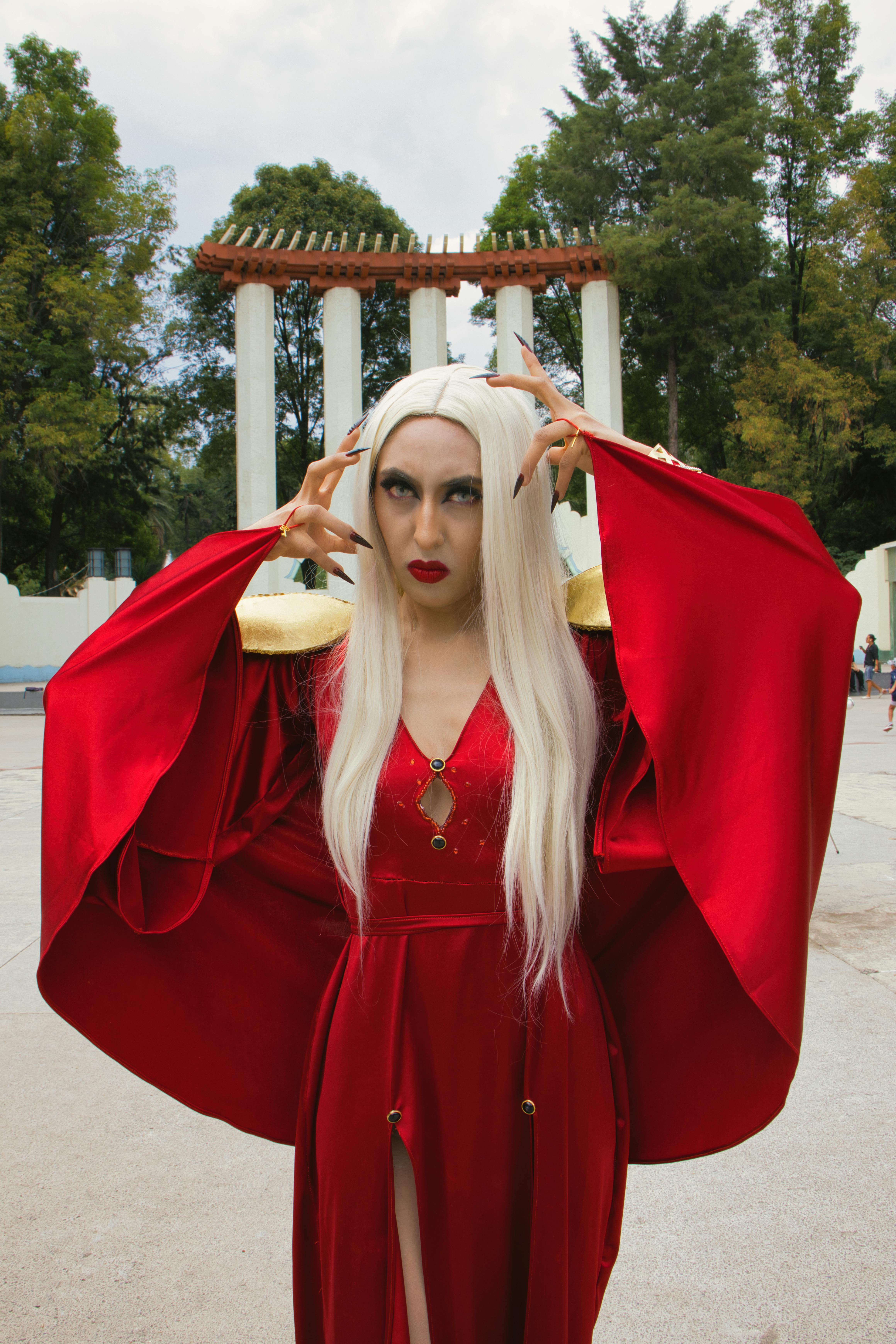 Gratis Kvinne i slående rødt kostyme poserer utendørs med søyler i bakgrunnen. Arkivbilde