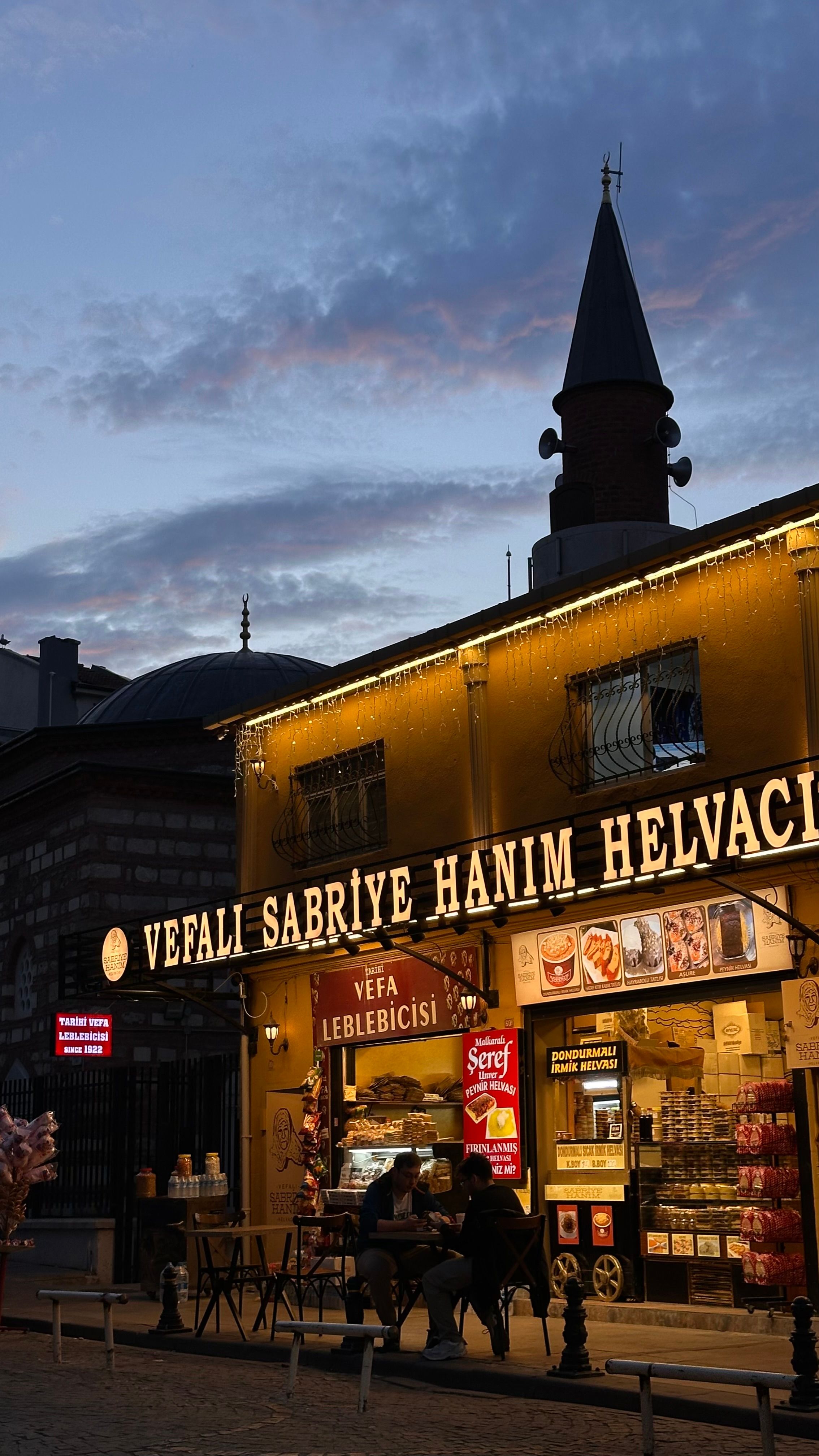 Nighttime view of a traditional Turkish sweet shop illuminated with warm lights.