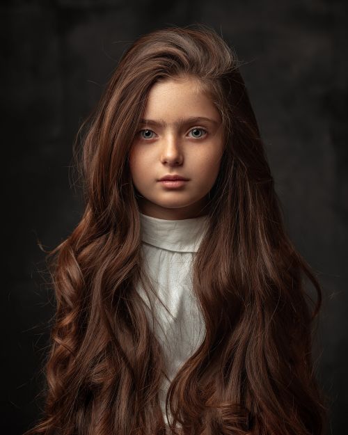 Free Captivating portrait of a young girl with long hair and deep gaze captured in a classic studio setting. Stock Photo
