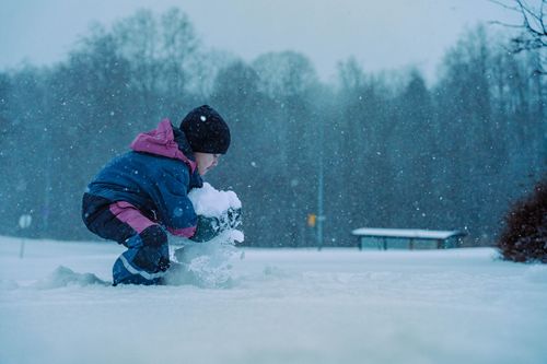 Free A child in winter attire playing with snow on a snowy day outdoors. Stock Photo