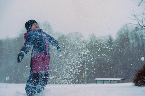 Free A joyful child in winter clothes playing in snow, surrounded by a serene snowy landscape. Stock Photo