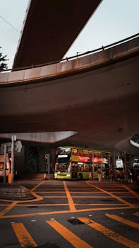 A vibrant urban scene showcasing a green double-decker bus under an overpass in Hong Kong.