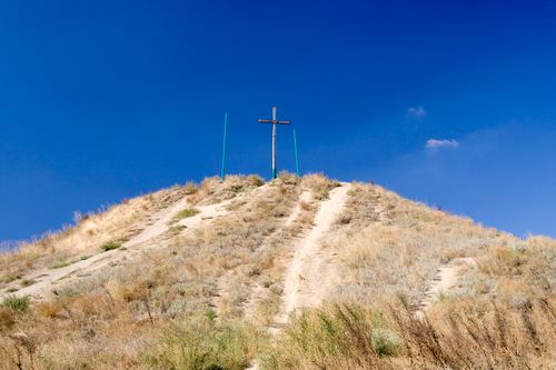 Free A lone wooden cross stands atop a hill under a vibrant, clear blue sky. Stock Photo