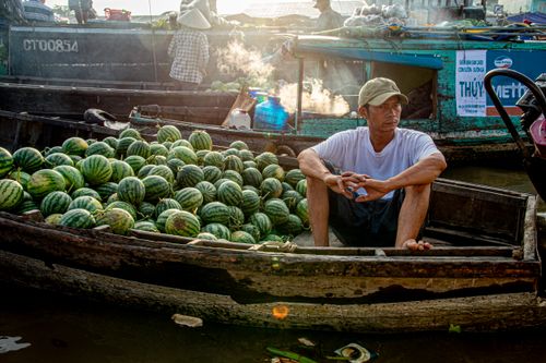 Free A vendor sells fresh watermelons from a wooden boat at a bustling floating market. Stock Photo