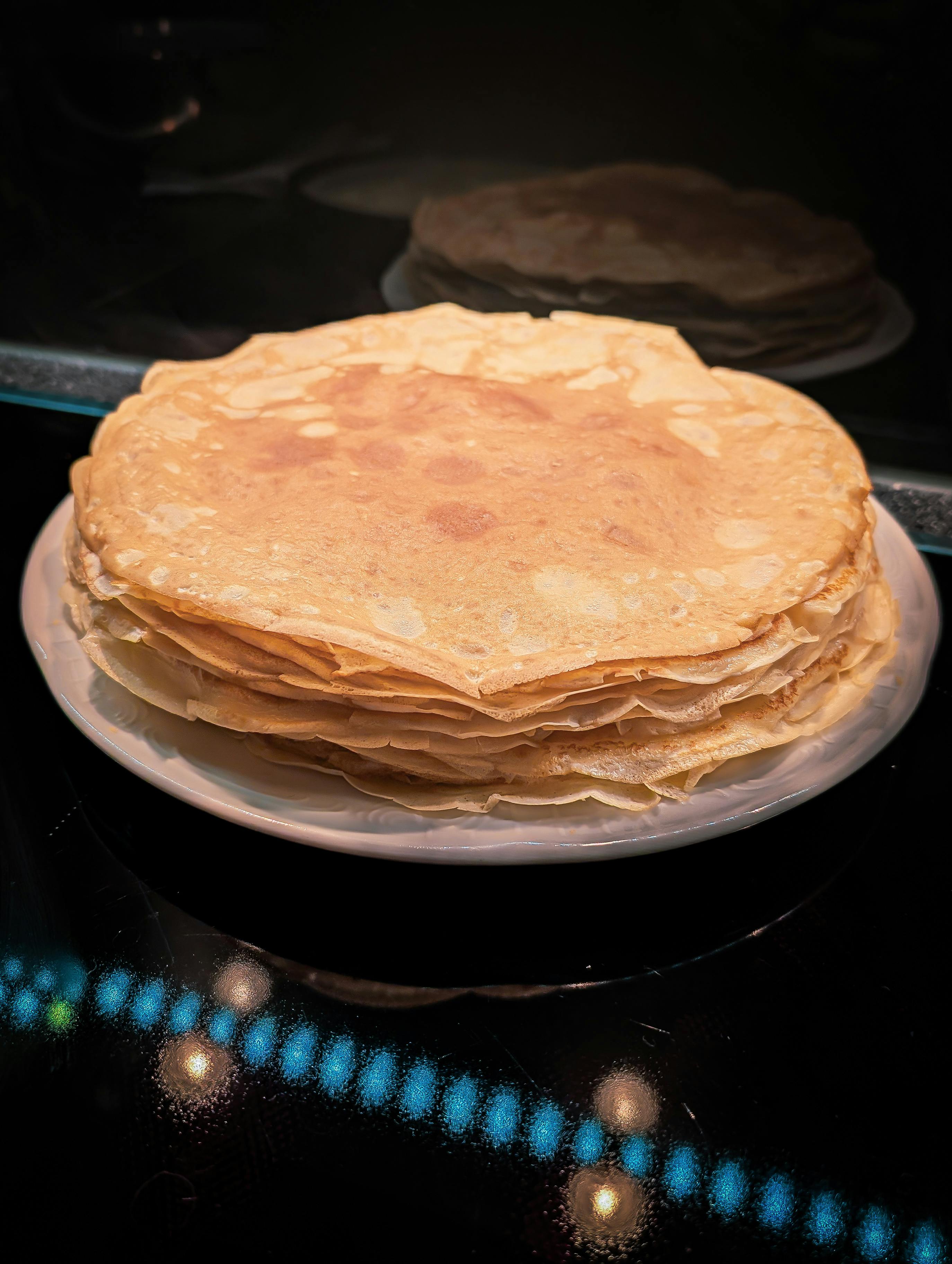 Deliciosa pila de crepes finas cuidadosamente dispuestas en un plato blanco, listas para servir.