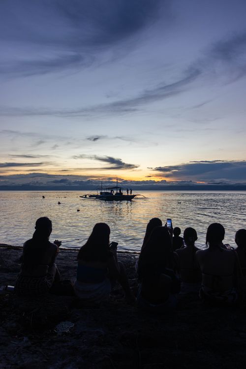 Free Silhouettes enjoying a stunning sunset on Moalboal beach with a banca boat in sight. Stock Photo