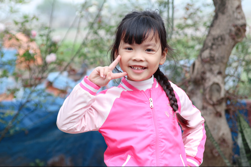 Free A cheerful young girl in a pink jacket gives a peace sign outdoors. Stock Photo