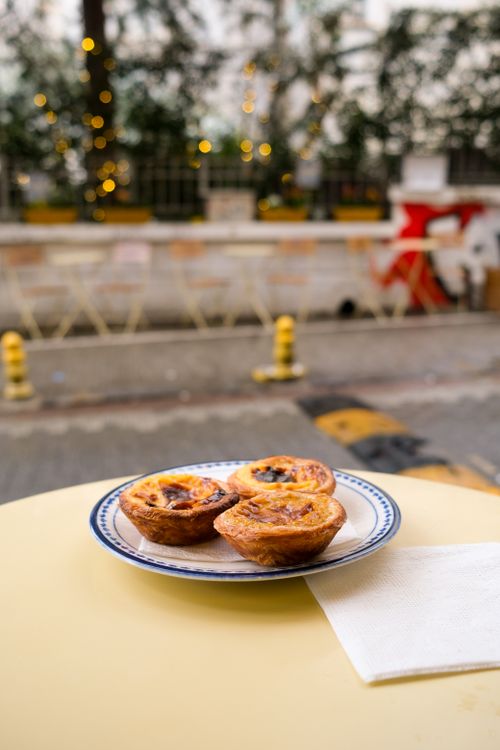 Free Three Portuguese custard tarts on a table outdoors with festive lights in the background. Stock Photo