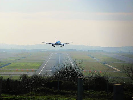 A commercial airplane descends on a runway during sunrise, captured from a distance.