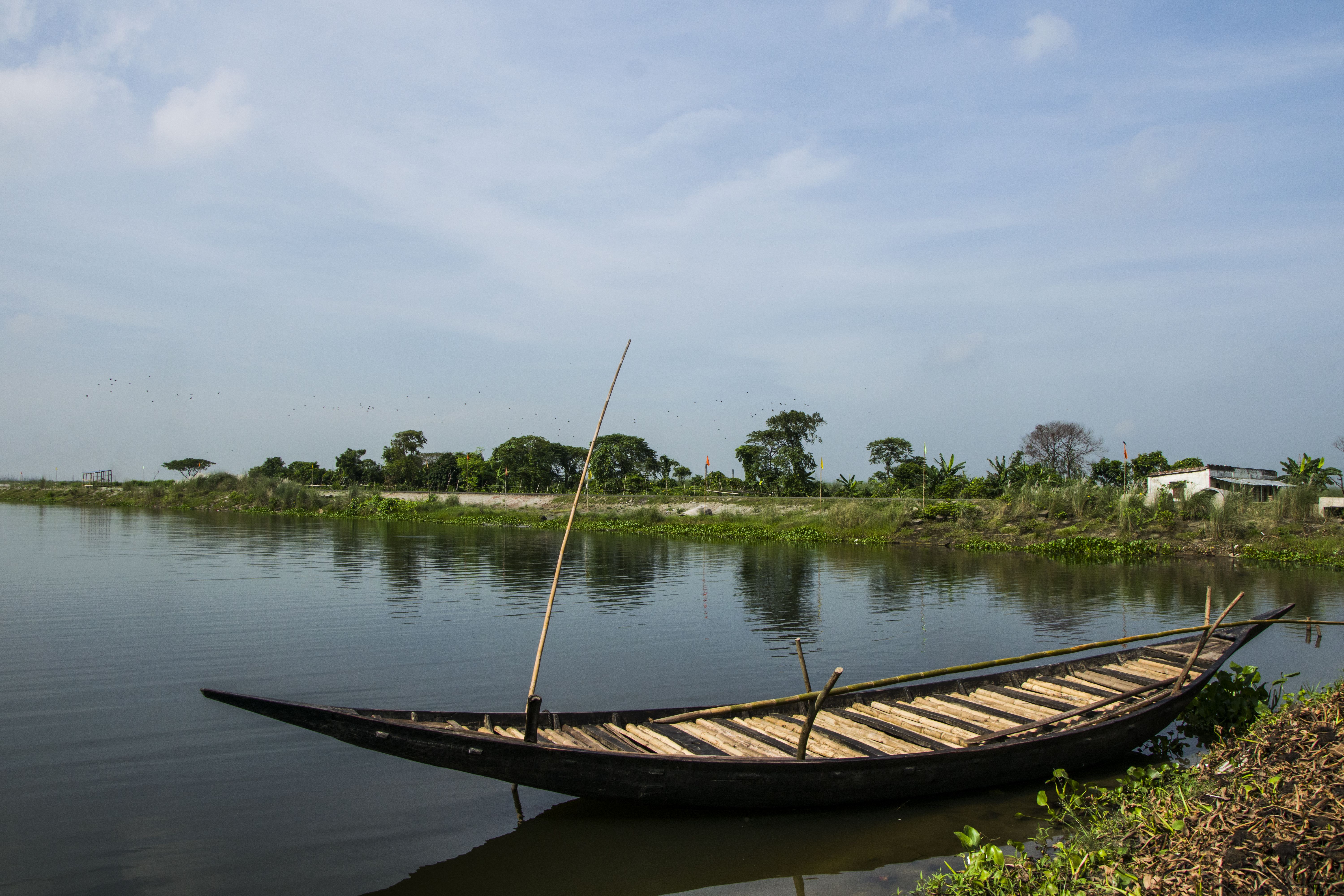 Free A peaceful scene of a traditional wooden boat on a calm river under a clear blue sky. Stock Photo