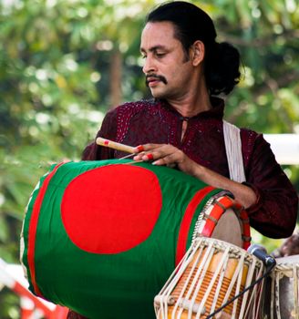 A musician in traditional attire playing a vibrant dhol drum outdoors.
