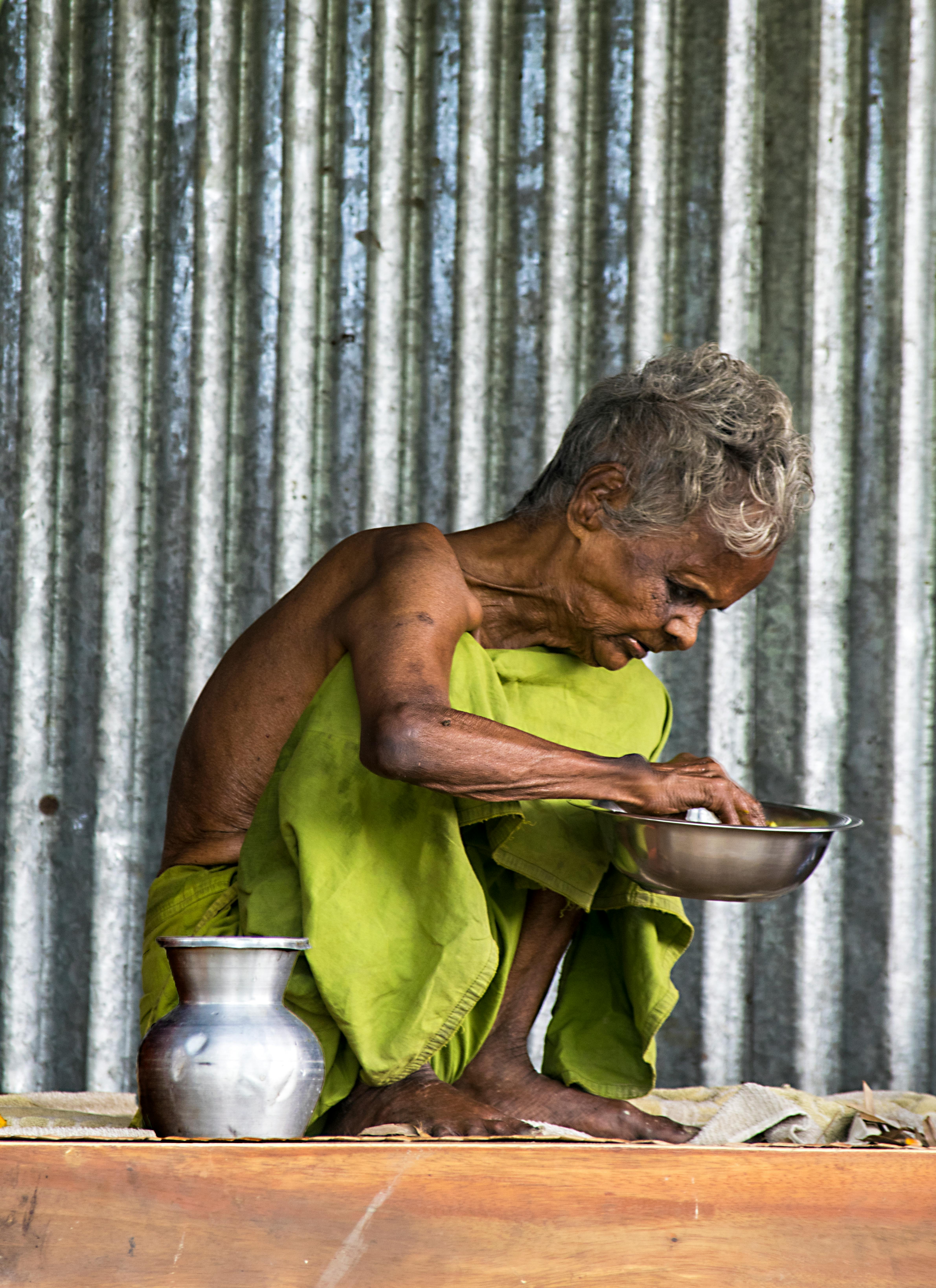 Gratis En eldre person i grønt antrekk tilbereder et måltid, og viser frem kulturell og tradisjonell livsstil. Arkivbilde