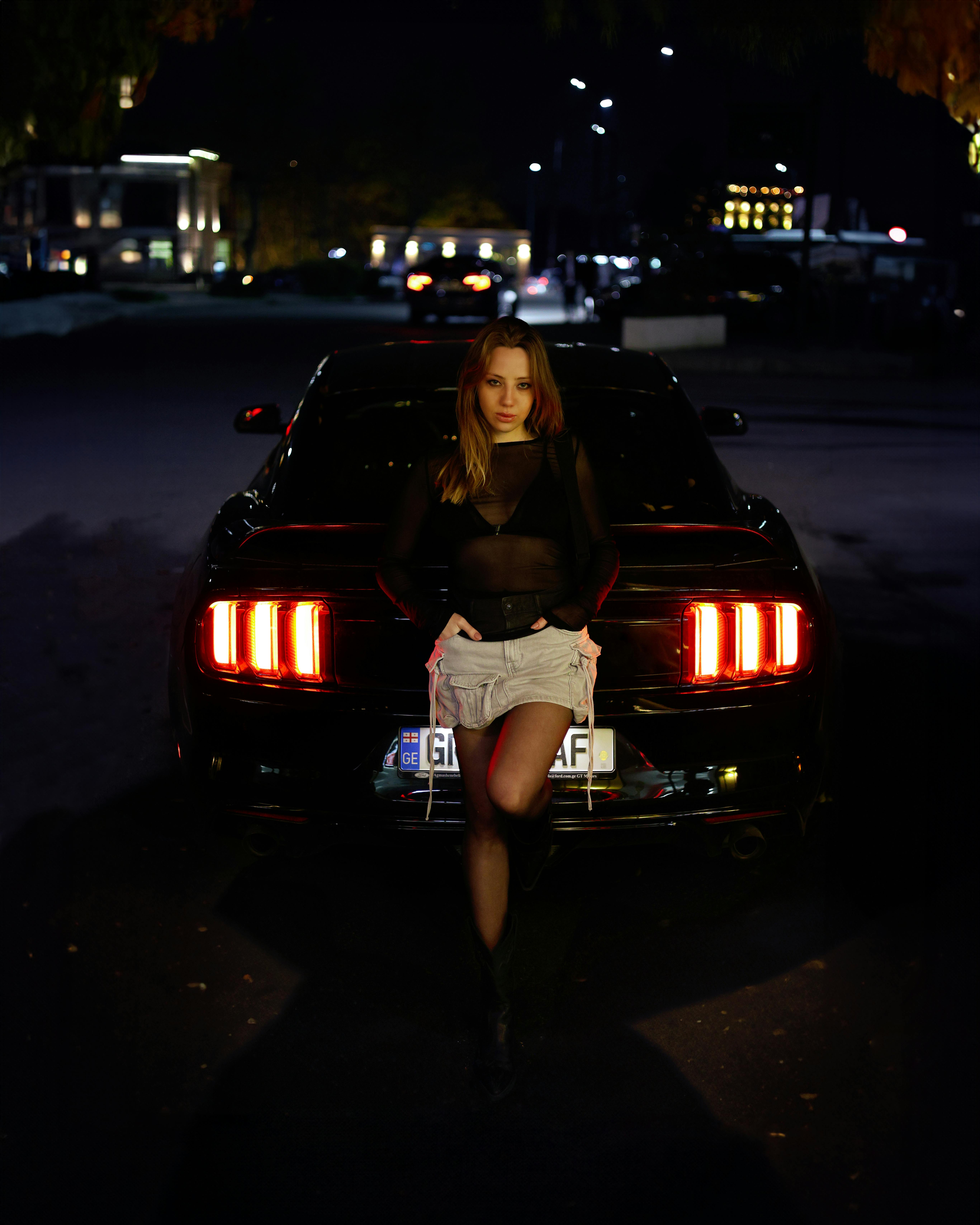 Kostenlos Stilvolles Model posiert nachts in einem urbanen Umfeld mit einem eleganten Auto und dramatischer Beleuchtung. Stock-Foto