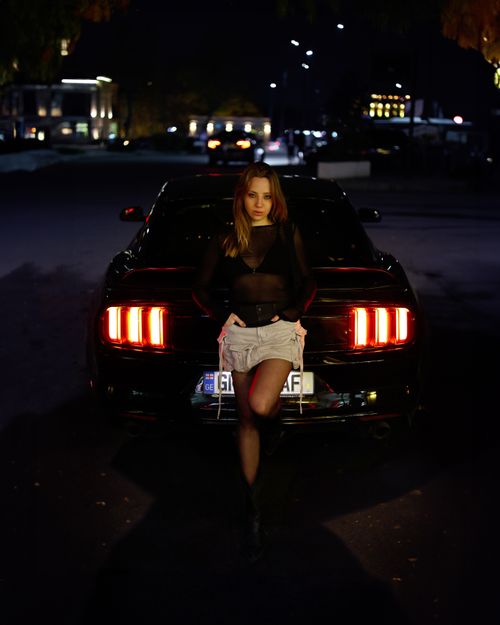 Free Stylish model posing at night in urban area with sleek car, dramatic lighting. Stock Photo