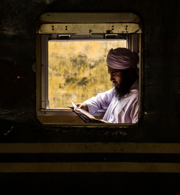 A man in a turban reads through a train window, illuminated by warm light.