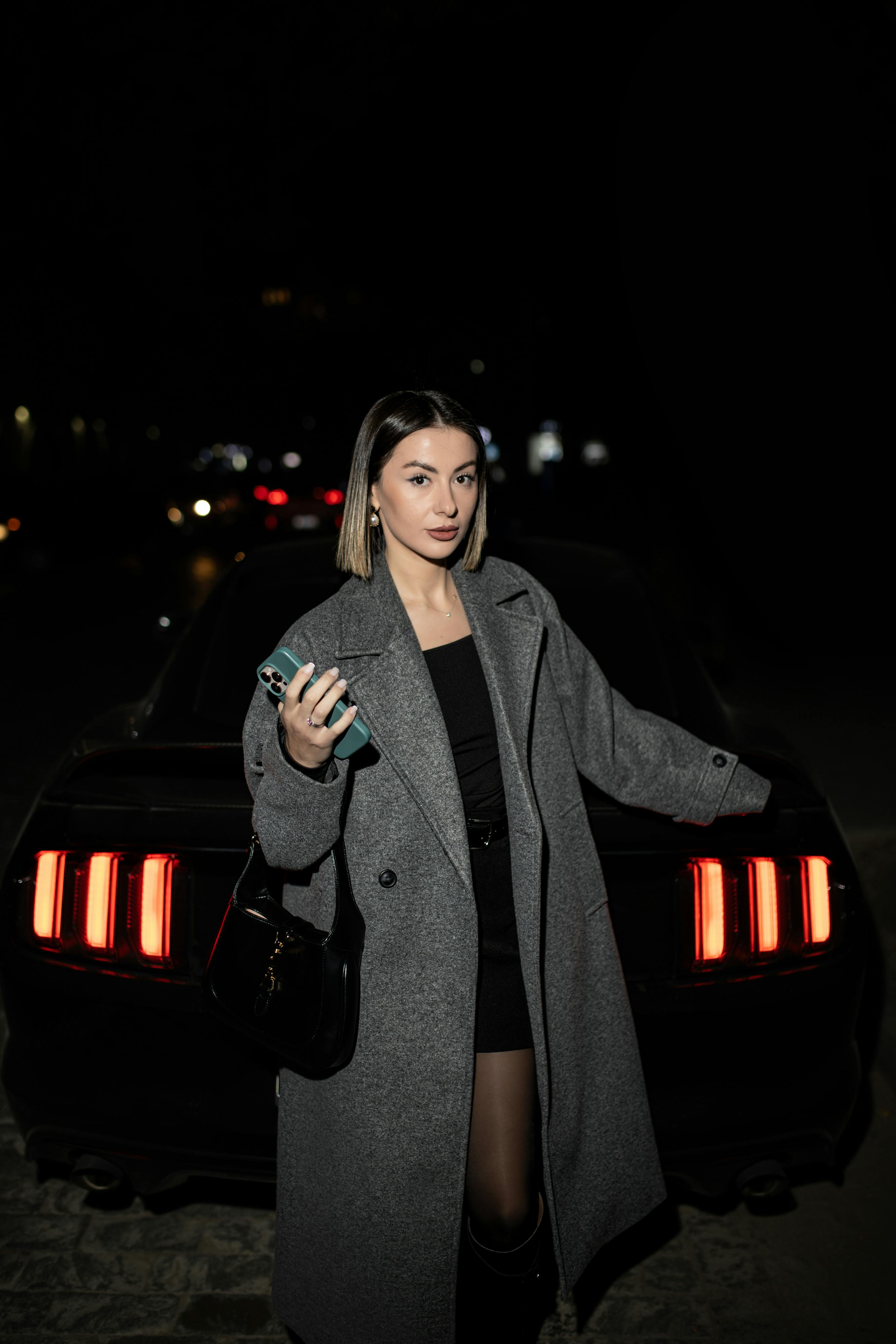 Gratis Una mujer de moda posa por la noche frente a un automóvil en el paisaje urbano de Tbilisi. Foto de stock