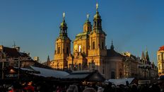 Beautiful view of the Church of St. Nicholas in Prague with festive market below at sunset.