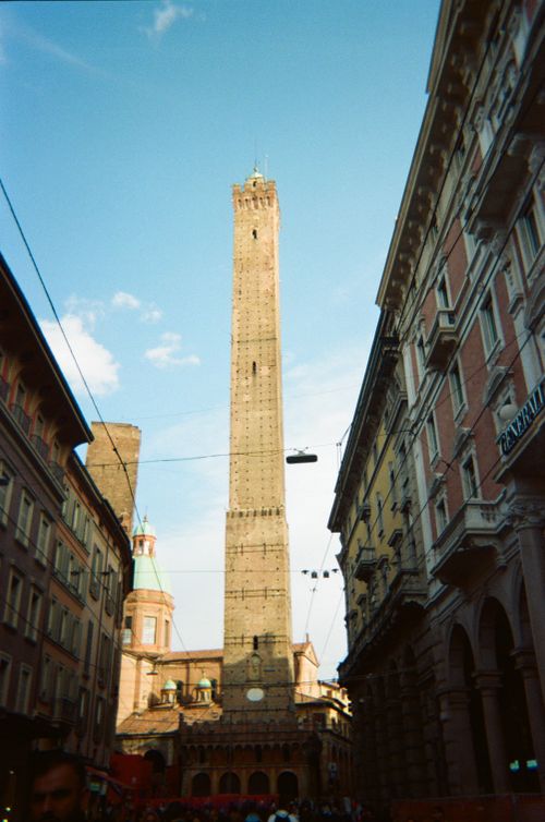 Free Iconic Torre Asinelli in Bologna, Italy framed by historic buildings under a clear sky. Stock Photo