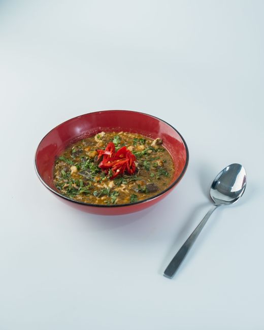 A bowl of pale yellow ground egusi seeds next to a handful of whole flattened melon seeds, with a wooden spoon resting nearby.