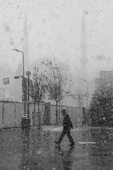Person walks in snowy cityscape, creating a serene black and white scene.