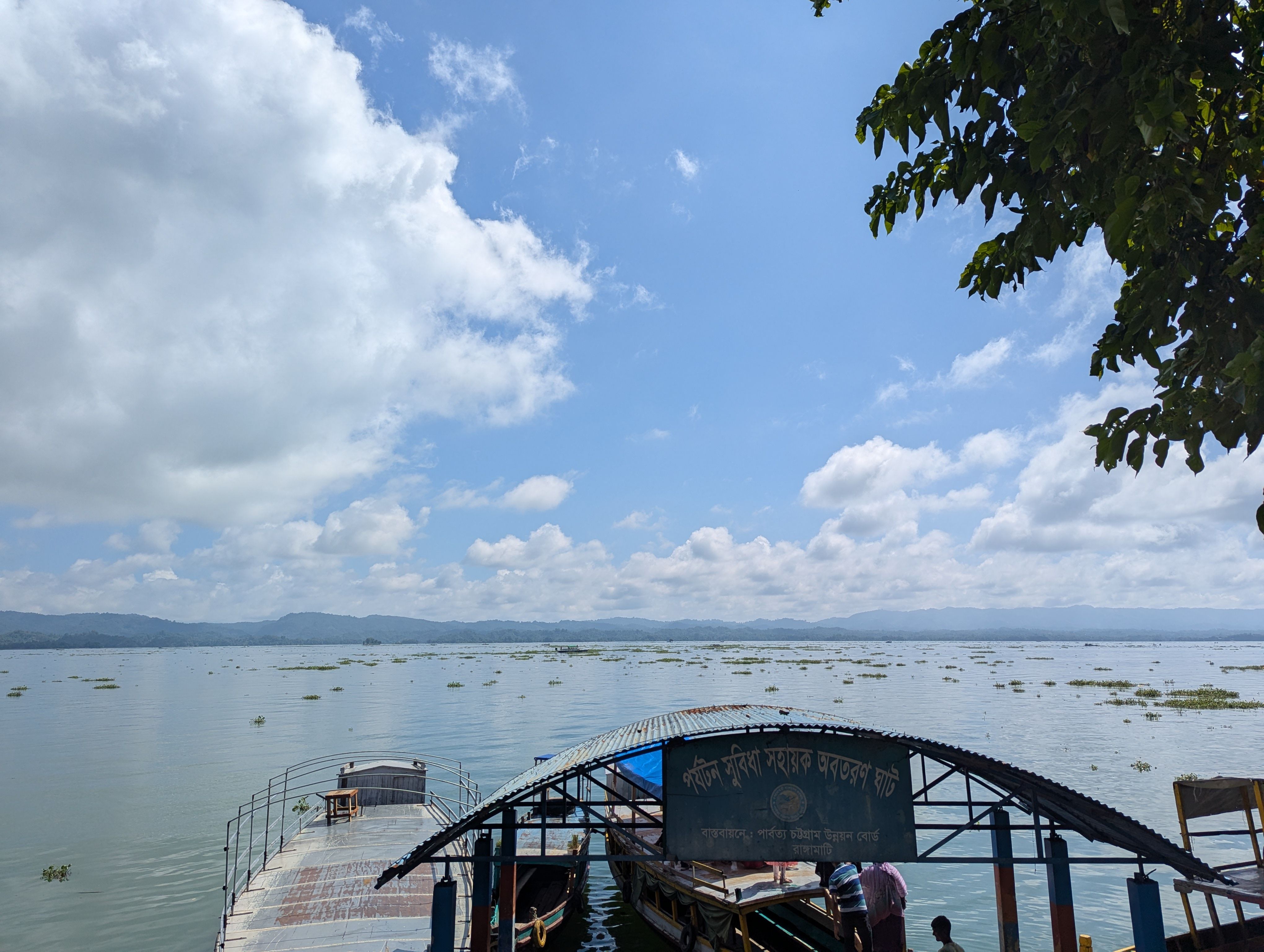 Scenic view of a tranquil lake with boats in Chittagong Division, Bangladesh under a blue sky.
