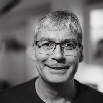 Close-up black and white portrait of a smiling man wearing glasses indoors.