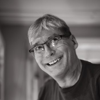Black and white portrait of a smiling senior man wearing glasses indoors.