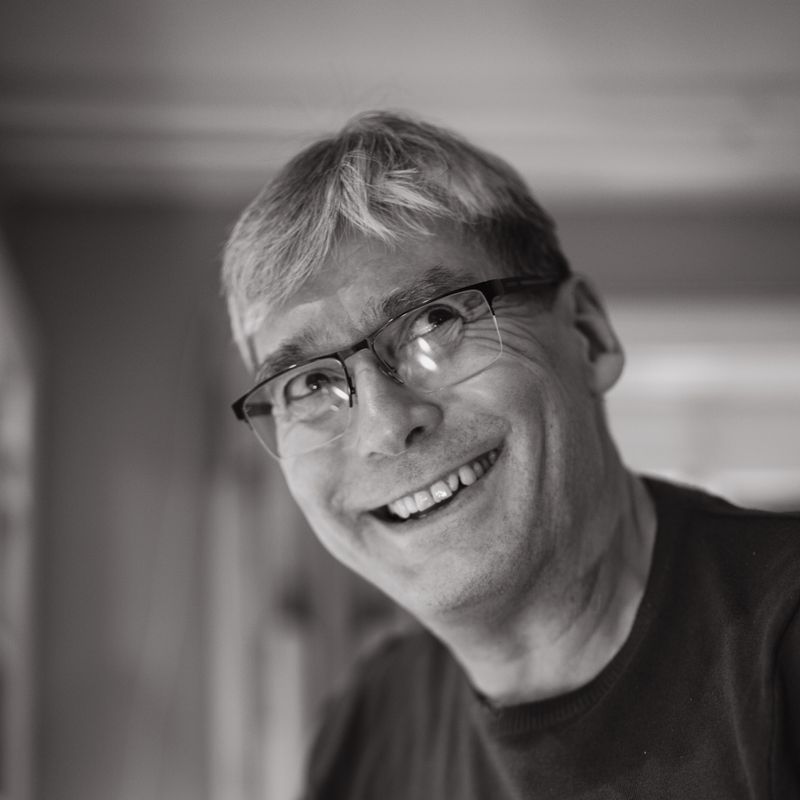 Black-and-white portrait of a smiling man in glasses — photo by Peter Platou on Pexels
