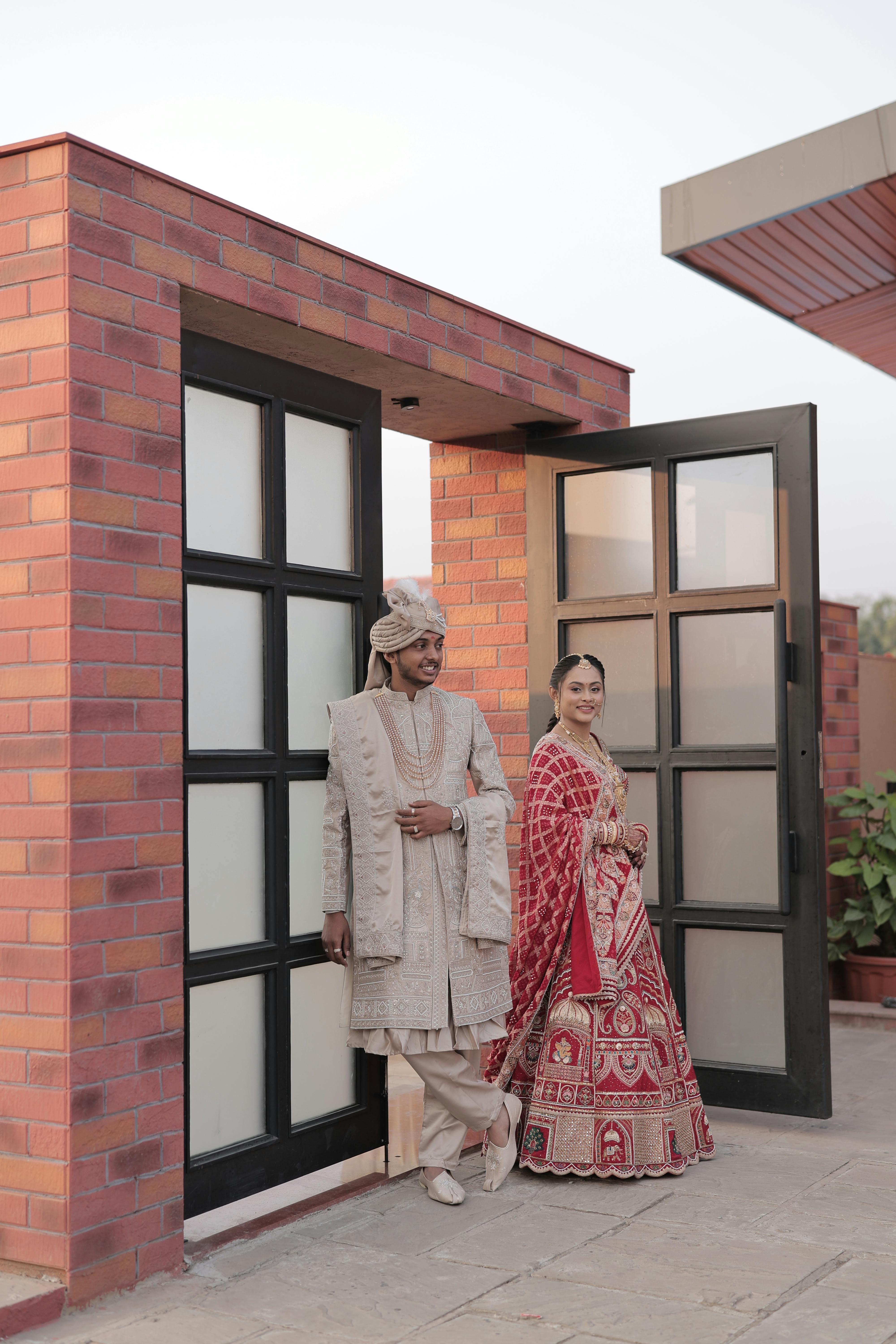Gratis Una pareja con el tradicional traje de boda indio posando frente a un edificio moderno. Foto de stock