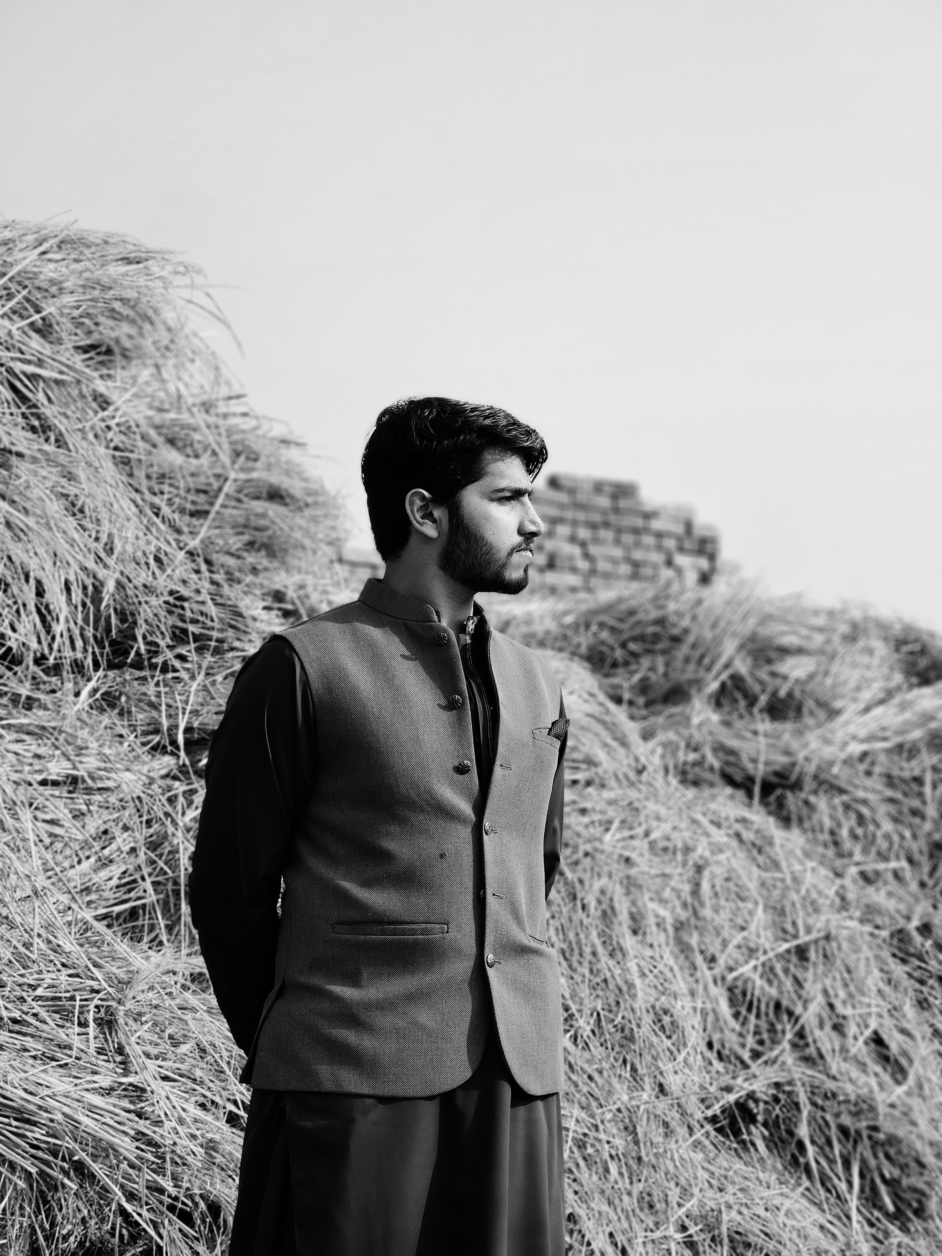 Stylish man in shalwar kameez and waistcoat stands outdoors, exuding elegance.