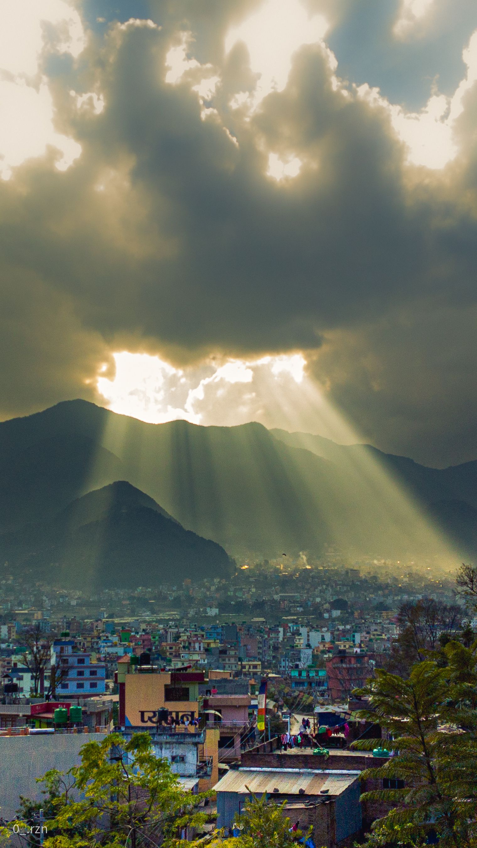 Captivating cityscape with sunbeams breaking through clouds over urban skyline.