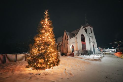 Free Snowy winter night with a beautifully lit Christmas tree beside a quaint church. Stock Photo
